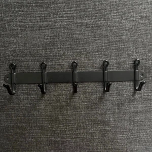 Metallhängare  - svart väggmonterad kroklist i metall med flera krokar. Den är i bra skick framtill, men har lite rost på baksidan som inte syns när den sitter uppe. 