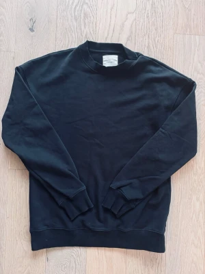 Svart sweatshirt från A Day’s March - En stilren svart sweatshirt från A Day’s March med rund halsringning och ribbade muddar vid ärmslut och nederkant. Tröjan är tillverkad i mjuk bomull och har en klassisk, avslappnad passform som funkar till allt.