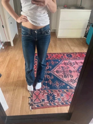 Mörkblå bootcut jeans med fickdetaljer - Säljer ett par mörkblå bootcut jeans med låg midja och snygga kontrastsömmar. Jeansen har dekorativa fickor bak. Perfekta för dig som gillar en avslappnad men trendig look.