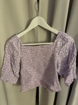 Ljuslila blommig croppad topp - Ljuslila croppad topp med små vita blommor och puffiga korta ärmar. Inte andvänd mycket alls, Från Kappahl i storlek 158/164
