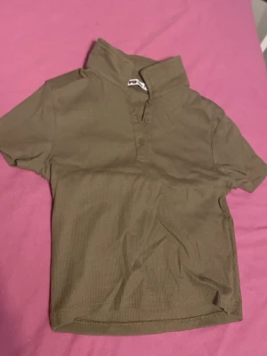 Olivgrön pikétröja från FB Sister - Jag har aldrig haft på mig den här kortärmade tröjan. Den är olivgrön pikétröja köpt från New Yorker med märket FB sister. Den har ribbad struktur och klassisk krage. Tröjan har knappar framtill och är gjord i ett mjukt, stretchigt material som känns bekvämt. Jag använde inte den eftersom de blev ett onödigt köp