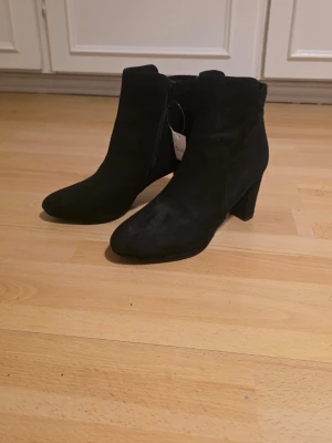Svarta mockastövletter med klack - Snygga svarta stövletter i mocka med medelhög klack och spetsig tå. Dragkedja på insidan för enkel på- och avtagning. Aldrig använda. Lapp sitter kvar