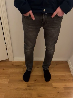 Grå slim fit jeans från Levi's - Säljer ett par grå slim fit jeans från Levi's med klassiska fem fickor och diskret logga på bakfickan. Jeansen har en snygg tvättad look och sitter tajt hela vägen ner. Perfekta för dig som gillar en stilren och avslappnad vibe. Skriv för mer info 