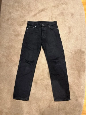 Svarta raka jeans från Weekday i modellen Barrel - Säljer ett par svarta jeans från Weekday med rak passform och fem fickor instinkten 28/30. Jeansen har klassisk design med knapp och dragkedja framtill samt silverfärgade nitar. Pris kan diskuteras!! Vid minsta fundering är det bara att höra av sig!