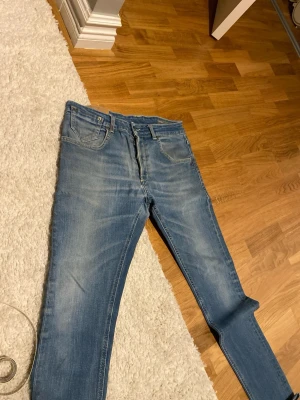 Ljusblå slim fit jeans - Säljer ett par ljusblå slim fit jeans med klassisk femficksdesign och dragkedjegylf. Jeansen har en tvättad look med snygga slitningar och smal passform. Perfekta för en avslappnad och trendig stil.