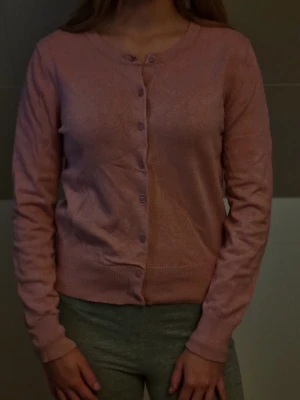 Ljusrosa kofta med knappar - Söt ljusrosa kofta med rund halsringning och knäppning framtill. Långa ärmar och ribbade muddar vid ärmslut och nederkant. Perfekt att slänga över en topp för en chill look. 