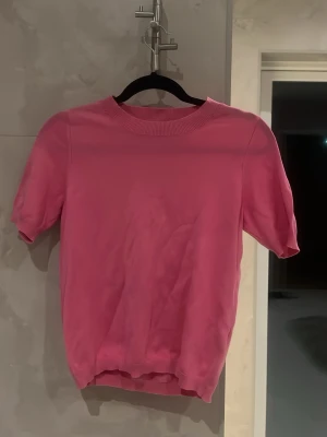 Rosa topp från Lindex - Snygg rosa topp från Lindex med rund halsringning och korta ärmar. Tillverkad i mjukt material som känns skönt mot huden. Perfekt att styla med jeans eller kjol för en fräsch look.