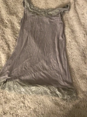 Grått nattlinne med spetsdetaljer - Mysigt grått nattlinne med breda spetsdetaljer vid halsringning och nederkant. Tunt och mjukt material som känns skönt mot huden. Perfekt för avslappnade kvällar hemma.