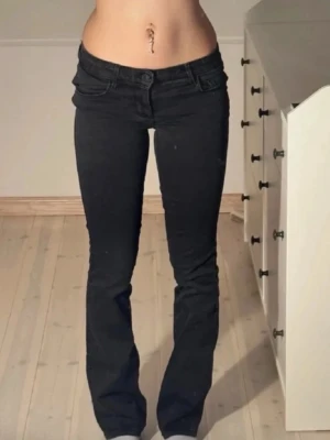 Svarta bootcut jeans - Säljer ett par svarta bootcut jeans med klassisk femficksdesign och normal midja. Jeansen har en lätt utsvängd passform nedtill och stängs med knapp och dragkedja. Perfekta för dig som gillar en tidlös och enkel stil.
