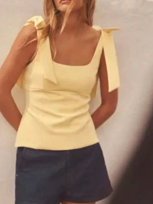 Gul linnetopp med rosettband - Söt ljusgul linnetopp med breda axelband som knyts i rosetter. Toppen har en rak, figurnära passform och fyrkantig ringning. Perfekt för varma dagar och ger en fräsch look till din outfit.
