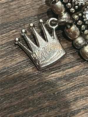 Silverfärgat halsband med blomma - Unikt halsband från Mariana i silverfärg med en stor blomformad hängare dekorerad med blå sten i mitten. Kedjan är grov och har en kronformad detalj nära låset. Perfekt för dig som gillar statement-smycken och cool design.