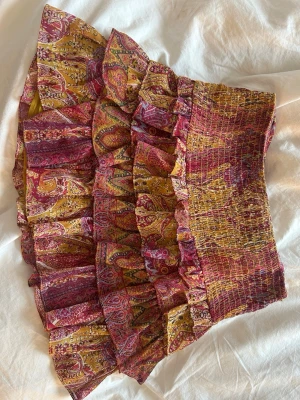 Mönstrad volangkjol i gult och rött - Eftertraktad Kort kjol med flera volanger i ett färgstarkt paisleymönster i gult, rött och rosa.   