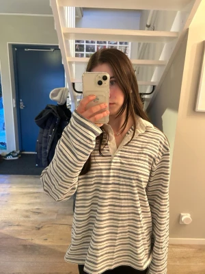 Randig långärmad tröja med krage - Säljer en vit och blå randig långärmad tröja  med krage. Skjortan har en avslappnad passform och är tillverkad i mjukt bomullstyg. Perfekt för en chill och stilren look.