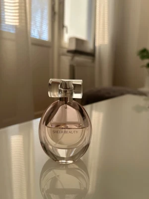Calvin Klein Sheer Beauty parfym - Calvin Klein Sheer Beauty parfym i en elegant, rund glasflaska med ljusrosa doft och transparent lock. Flaskan har en modern och stilren design som känns både fräsch och feminin. Perfekt för dig som gillar lätta och fräscha dofter.