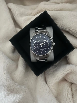 Citizen silverfärgad kronografklocka - Stilren klocka från Citizen med silverfärgad länk i metall och mörkblå urtavla. Klockan har kronograffunktion, datumvisning och tydliga markeringar. Perfekt accessoar för dig som gillar klassisk och modern stil.