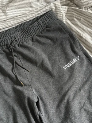Mörkgrå mjukisbyxor från Gymshark - Snygga mörkgrå mjukisbyxor från Gymshark med smal passform och dragsko i midjan. Byxorna har elastisk midja, sidofickor och är tillverkade i mjukt bomullsmaterial. Perfekta för chill eller träning.