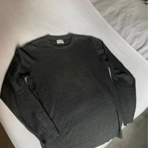 Mörkgrå stickad tröja A Day's March - Snygg mörkgrå stickad tröja från A Day's March i en blandning av ull. Tröjan har rund halsringning, långa ärmar och ribbade muddar vid ärmslut och nederkant. Perfekt för lager-på-lager och enkel att matcha med olika outfits.  Enda defekten är det lilla hålet vid ryggen men går att fixa enkelt hemma !