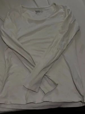 Vit långärmad topp från Basic - En enkel och stilren vit långärmad topp från Basic. Modellen har rund halsringning och är tillverkad i mjuk bomull, perfekt för en clean och avslappnad look. Passar till allt och är ett måste i garderoben.