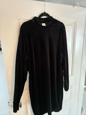 Svart sammetsklänning från H&M - En svart sammetsklänning från H&M med lång ärm och rak passform. Klänningen har en enkel design med rund halsringning och är tillverkad i mjuk sammet, vilket ger en lyxig känsla. Perfekt för dig som gillar stilrena plagg med en twist. Passar L snarare än XL