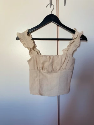 Beige croppad linnetopp med volang - Söt beige croppad linnetopp med breda axelband och volangdetaljer.