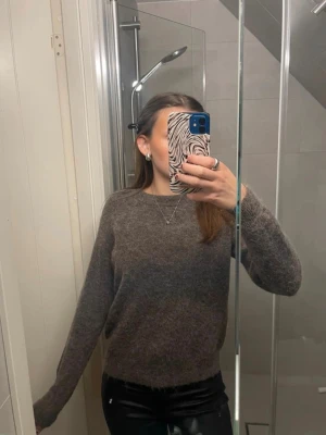 Mörkbrun stickad tröja - En enkel och stilren mörkbrun stickad tröja med rund hals och långa ärmar. Tröjan har en mjuk och lite luddig yta, perfekt för att hålla sig varm. Passar bra till jeans eller skinnbyxor för en avslappnad look. Storlek S men passar en XS.