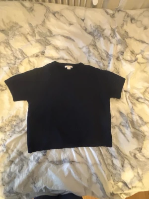 Svart stickad tröja från Gina Tricot - En svart stickad tröja från Gina Tricot med rund halsringning och korta ärmar. Tröjan har en enkel och stilren design, perfekt att matcha med jeans eller kjol. Mjuk och skön att ha på sig.