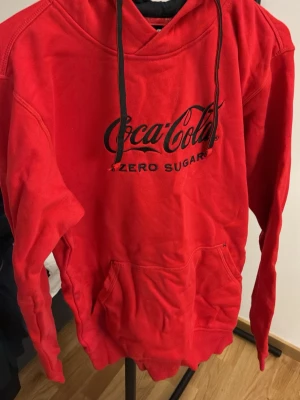 Röd Coca-Cola Zero hoodie • Herr • M - Cool och ikonisk röd hoodie med Coca-Cola Zero Sugar-logga i svart på bröstet. Hoodien har en stor huva med svarta snören och magficka. Materialet är mjukt och bekvämt, perfekt för chill dagar. Faktiskt aldrig använt eller tvättat den, bara provat den en gång. Därav superfint skick. 
