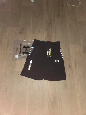Svarta Under Armour Shorts - Svarta Underarmour Medium shorts som funkar till gymmet,aktiviteter,löpning,etc.. De är helt nya och oanvända de har den original påsen som ni ser på bilden.