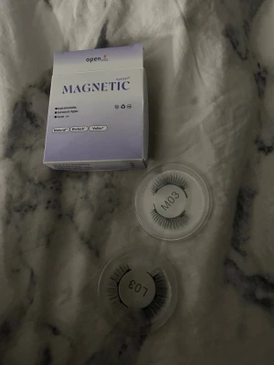 Magnetiska lösögonfransar Open - Säljer ett par magnetiska lösögonfransar från Open, modell L03. Fransarna är svarta och kommer i runda plastförpackningar. Perfekta för dig som vill ha naturlig eller fylligare look utan lim. Enkel applicering tack vare magnetteknik.