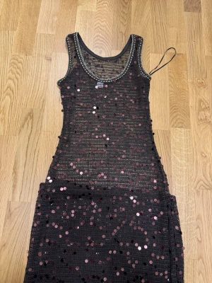 Svart paljettklänning med pärldetaljer - Snygg svart klänning täckt med glittriga paljetter och pärldetaljer vid halsringningen. Ärmlös modell med rund hals och figurnära passform. Perfekt för dig som vill sticka ut och glänsa lite extra. Perfekt under bikini eller till fest 