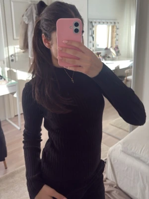 Svart ribbad tröja - Tajt svart ribbad polotröja med lång ärm och hög hals. Tröjan har en stilren och enkel design som passar till det mesta. Materialet ser ut att vara mjukt och stretchigt, vilket gör den bekväm att bära.