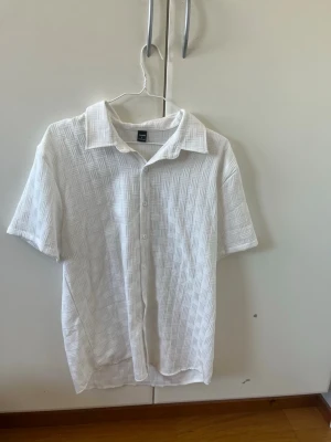 Vita shorts med strukturmönster - Säljer ett par vita shorts från H&M med snyggt strukturmönster och elastisk midja med snörning och en vit piké att matcha med. Materialet känns mjukt och luftigt, perfekt för varma dagar. Designen är enkel men modern.