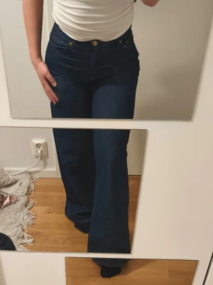 Mörkblå bootcut jeans - Säljer ett par mörkblå bootcut jeans med hög midja och klassisk femficksdesign. Jeansen har vida ben och stängs med dragkedja och knapp. Perfekta för dig som gillar en retroinspirerad look och vill ha ett par jeans som sitter snyggt över höfterna.