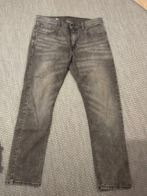 Grå Levi's 502 jeans med raka ben - Säljer ett par gråa Levi's 502 jeans med raka ben och klassisk femficksdesign. Jeansen har en snygg tvättad look, Levi's patch bak och råa kanter vid bensluten. Perfekta för dig som gillar en avslappnad men stilren vibe.