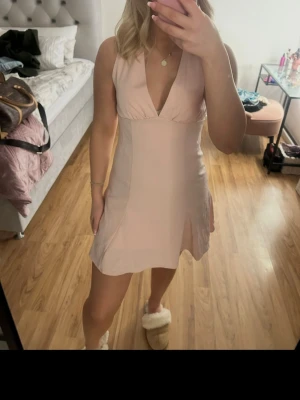 Ljusrosa kort klänning med v-ringning - Supersöt ljusrosa kort klänning med djup v-ringning och ärmlös design. Klänningen har en lätt utsvängd kjol och markerad midja som ger en feminin siluett. Perfekt för sommarens alla tillfällen. Materialet känns mjukt och följsamt. Klänningen är från cider och är i väldigt fint skick, använd ett fåtal gånger.