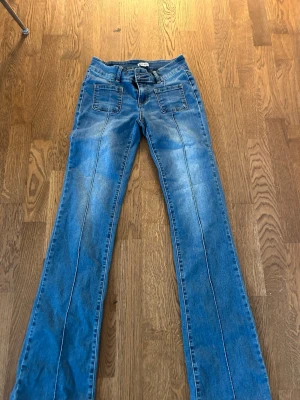 Blå bootcut jeans från Madlady - Säljer ett par blå bootcut jeans från Madlady i storlek EU34/Tall. Jeansen har raka ben med markerade sömmar framtill och två stora fickor på framsidan. Klassisk denimlook som är perfekt för dig som gillar en trendig och avslappnad stil.