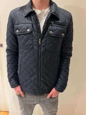 Jack & Jones jacka blå - Säljer en mörkblå quiltad Jack & Jones jacka med dragkedja och knappar på bröstfickorna. Storlek S