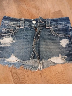 Blå slitna jeansshorts med fransar - Säljer ett par blå jeansshorts med slitna detaljer och fransig kant. Klassisk femficksmodell med knapp och dragkedja framtill. Perfekta för sommaren och ger en avslappnad vibe.