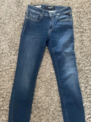 Mörkblå jeans från Replay - Snygga mörkblå jeans från Replay med klassisk femficksmodell och diskreta slitningar. Jeansen har smal passform och är tillverkade i stretchigt denimtyg för extra komfort. Perfekta för en trendig och avslappnad stil.