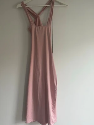 Ljusrosa långklänning med öppen rygg - Säljer en ljusrosa långklänning med breda axelband som korsas i ryggen och en snygg draperad öppen rygg. Materialet känns mjukt och följsamt. Storlek xs/s