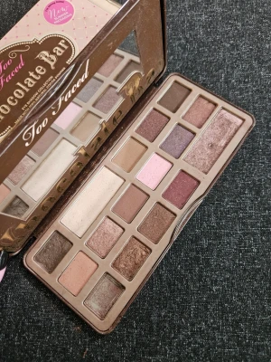 Too Faced Chocolate Bar ögonskuggspalett - Ikonisk ögonskuggspalett från Too Faced med 16 nyanser i bruna, rosa, lila och guldiga toner. Paletten har både matta och skimriga skuggor i rektangulära och fyrkantiga pans. Förpackningen är brun och formad som en chokladkaka med spegel i locket.