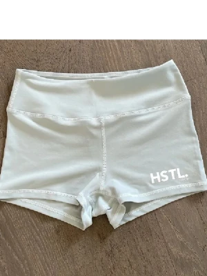 Ljusgråa träningstights från HSTL - Supersnygga ljusgråa shorts från HSTL med hög midja och kort passform. Perfekta för träning eller gymmet. Tillverkade i mjukt och stretchigt material som ger bra rörelsefrihet. Diskret logga framtill på benet.