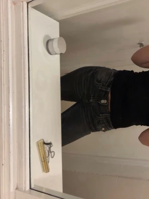 Svarta lågmidjade bootcut jeans  - Säljer ett par svarta/mörk gråa bootcut jeans med låg midja och en söt liten ficka fram. Jeansen har en snygg tvättad look och silverfärgade knappar. Passar perfekt till en avslappnad och trendig stil. Jeansen är i storlek 164, passar som XS. 