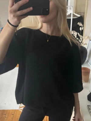Svart oversized stickad tröja - En svart stickad tröja med oversized passform och korta ärmar. Tröjan har rund halsringning och är gjord i ett mjukt material som ger en avslappnad look. Perfekt att matcha med jeans eller byxor för en cool stil.