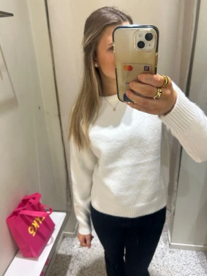 Vit stickad tröja med rund hals - En enkel och stilren vit stickad tröja med rund hals och ribbade muddar vid ärmslut och nederkant. Perfekt att matcha med jeans eller kjol för en clean look. Materialet ser ut att vara mjukt och bekvämt.