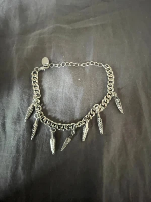 Kedjearmband med silverfärgade spikes - Snyggt armband i silverfärgad metall med grov kedja och sju hängande spikes som ger en edgy vibe. Perfekt för dig som gillar statement-smycken och vill sticka ut lite extra. Justerbar längd med karbinlås.
