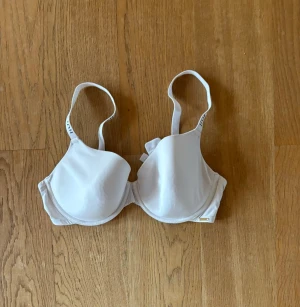 Vit bygel-bh från Lindex 85C - Säljer en vit bh från H&M med bygel och vadderade kupor. Bh:n har justerbara axelband och hakknäppning bak. Tillverkad i ett mjukt material och märkt med Sustainable Choice. Enkel och stilren design.