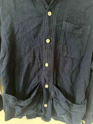 Mörkblå overshirt från Zara - Stilren mörkblå overshirt från Zara med klassisk krage, vita knappar och tre fickor framtill. Tillverkad i ett mjukt, strukturerat tyg som ger en avslappnad look. Perfekt att bära öppen över en t-shirt eller stängd som skjorta.Det behöver bara strykas. 