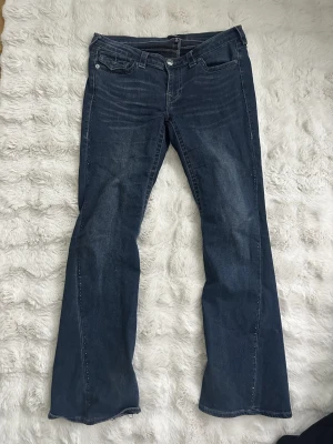 Blå flared jeans från True Religion - Säljer ett par blå flared jeans från True Religion. Jeansen har låg midja och fickdetaljer bak. Den har också stenar på sidorna av benen..
