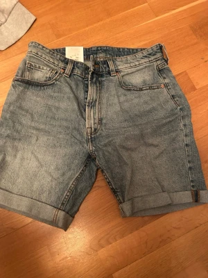 Blå jeansshorts från carlings - Klassiska blå jeansshorts från carlings med fem fickor, uppvikta benslut och dragkedjegylf. Tillverkade i slitstarkt denimtyg med en avslappnad passform. Perfekta för en casual och trendig look. Nya med lappen kvar